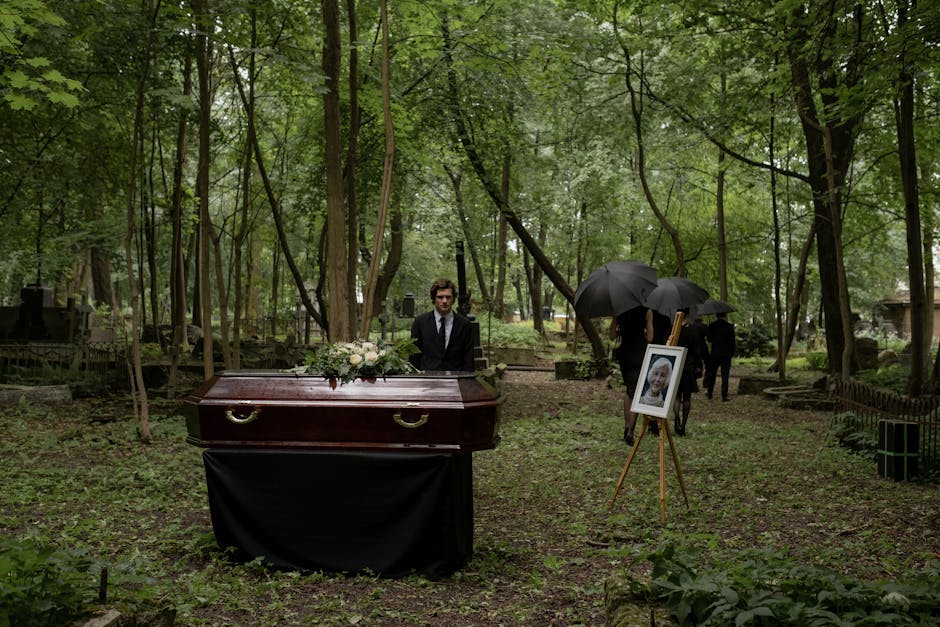A funeral ceremony in a wooded cemetery with a wooden coffin and mourners.