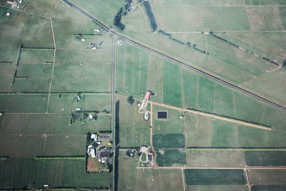 Aerial shot showcasing expansive green farmland with field boundaries and rural structures.