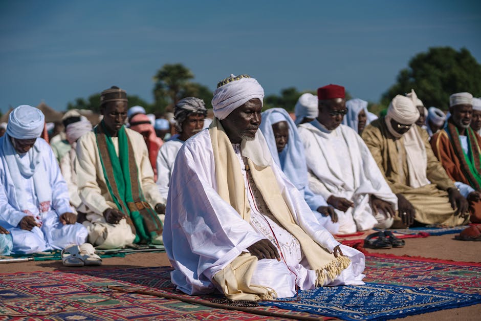 Group of men in traditional clothing engaged in Muslim prayer outdoors.