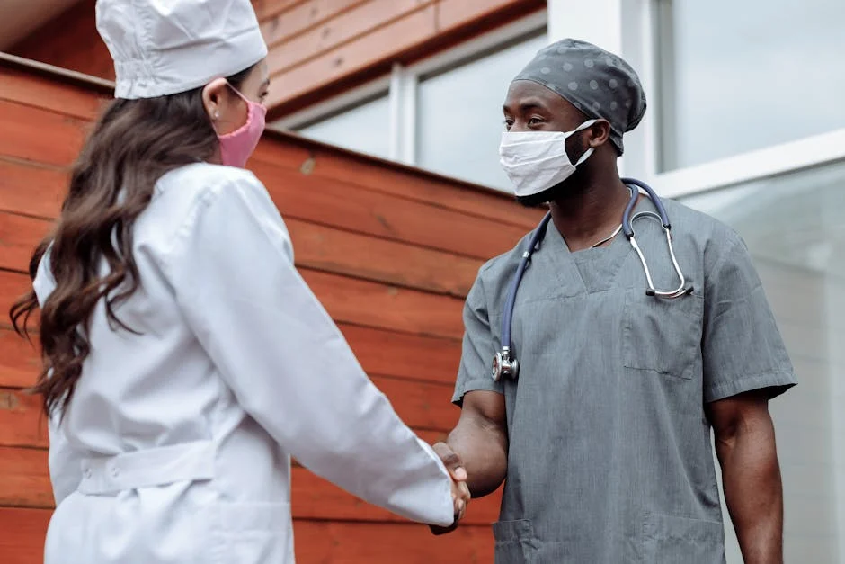 Two healthcare workers in face masks shaking hands outdoors, promoting teamwork and collaboration.